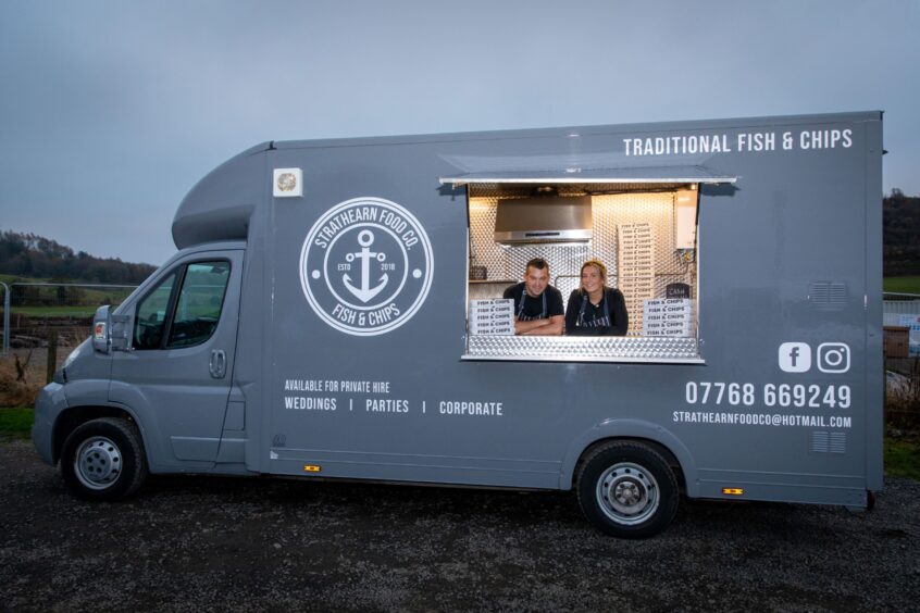 The Strathearn Food Company's slate grey fish and chips van with Steven and Daniella McPhee inside looking out.