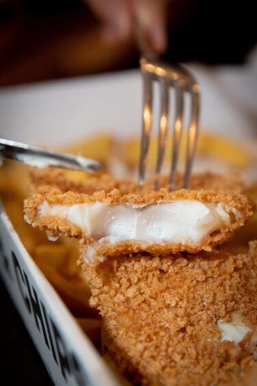 A close-up of breaded haddock in a fish and chips box.