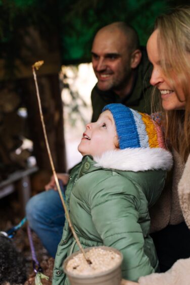 3-year-old Lily smiling at her sapling in the Greenman's den.