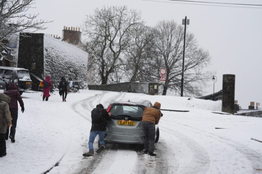 People help to push a vehicle uphill in the snow at Stirling. 