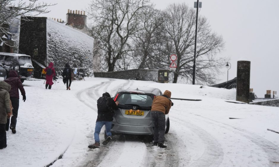 People help to push a vehicle uphill in the snow at Stirling.