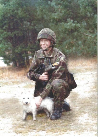 James Collinson in camouflage gear petting a west highland terrier