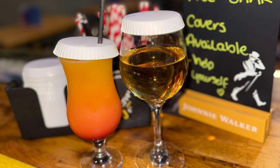 Two drinks on a table both with safety covers over them.