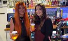 The two managers stand at the bar holding drinks with safety covers on them.