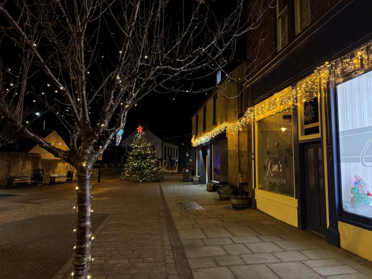 A tree lit up with fairy lights in front of a Coupar Angus street and Christmas tree