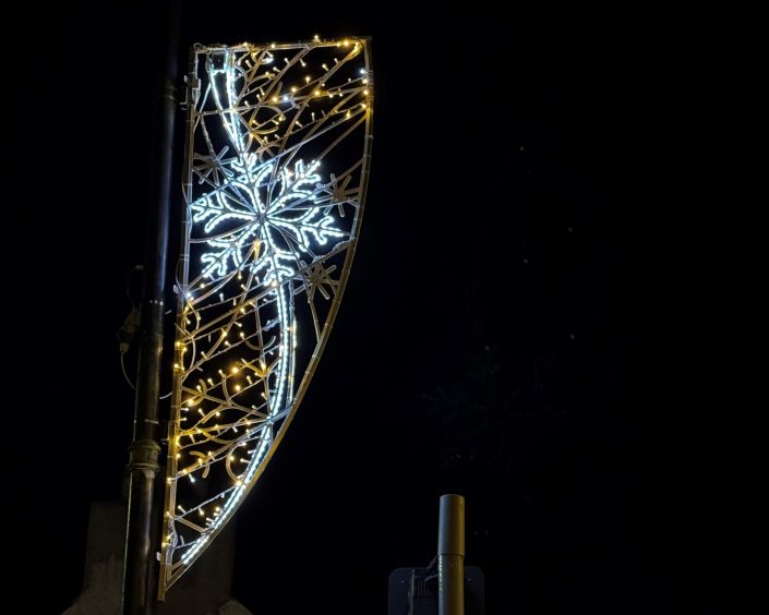 A lit up snowflake surrounded by twinkling lights and attached to a lamp post.