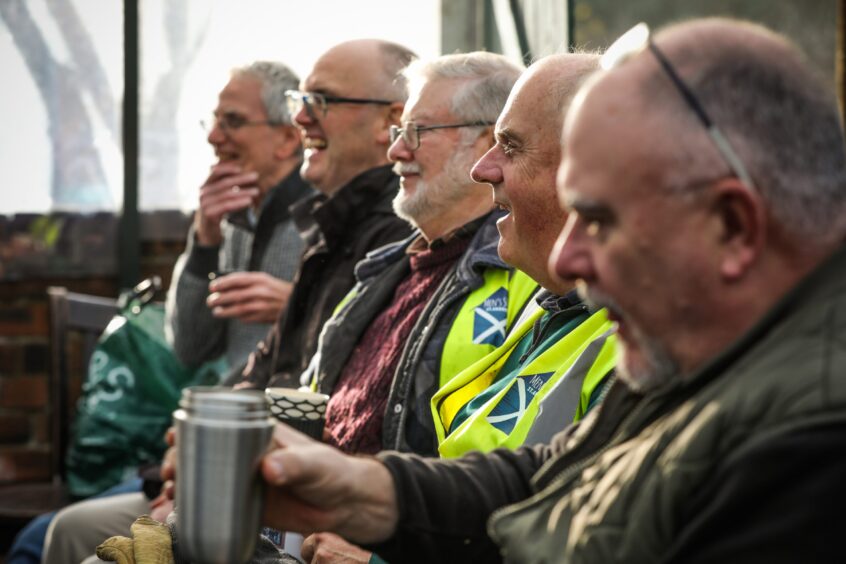 Image shows a group of older men sharing a joke during a tea break at St Andrews Men's Shed.