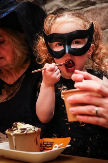 A little girl wearing a cat cat woman mask and spooning crumble into her mouth.