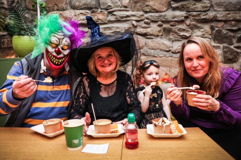 A family of four enjoying crumble at the Sweetpea Cafe dressed up for Halloween in a witch outfit, scary mask and cat costume.