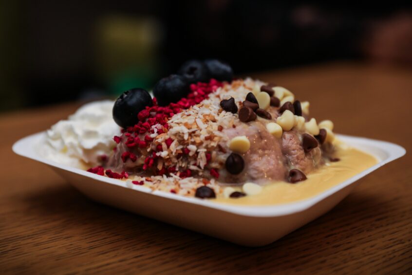 A huge blueberry cinnamon bun topped with cistard, blueberries, freeze dried strawberry pieces, coconut and chocolate chips.