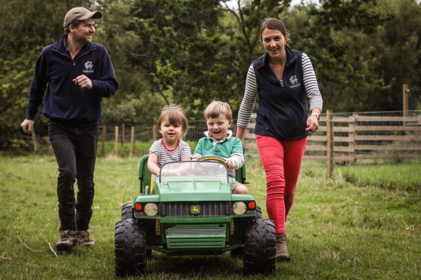 Tessa and Michael playing with their two children on the farm with a small kids farm vehicle.