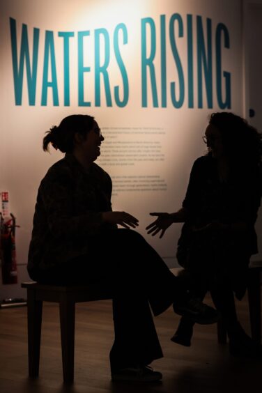 Two women talking in front of display with Waters Rising written in big blue letters behind