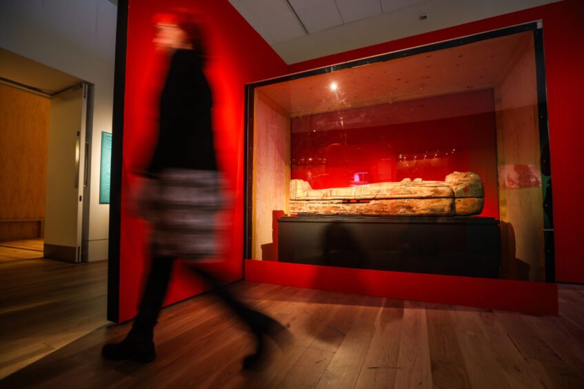 Person walking past sarcophagus in display case at Perth Museum