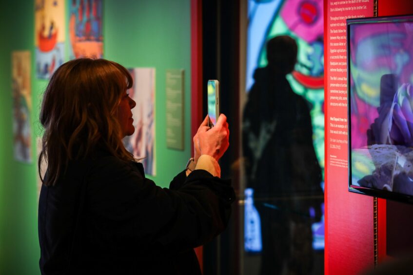 Woman with mobile phone taking photo of colourful paintings