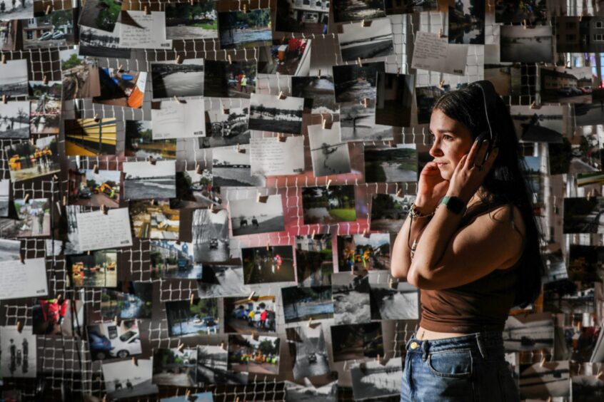 woman listening on headphones with wall of photos and postcards behind her