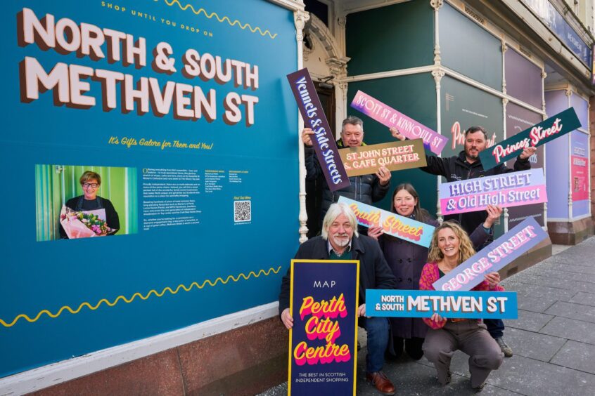 Shop keepers and council leader Grant Laing holding signs in front of a large North and South Methven Street billboard.