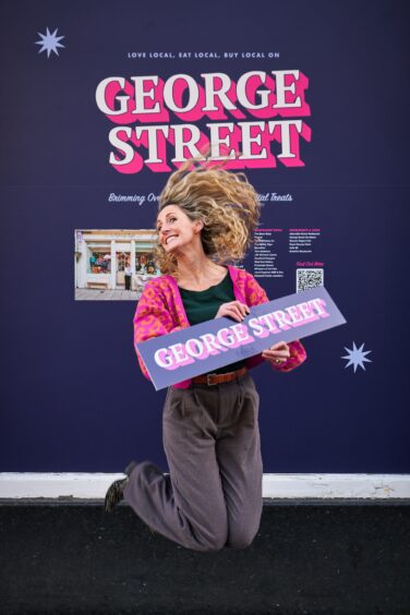 Linda Byers jumping for joy with a George Street sign