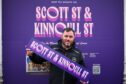 Justin Hy holding sogn for Scotti Street and Kinnoull Street in front of purple billboard