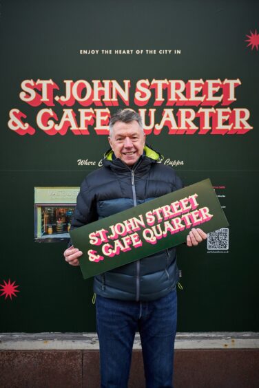 Steve McGilvray holding a 'St John Street and Cafe Quarter' sign