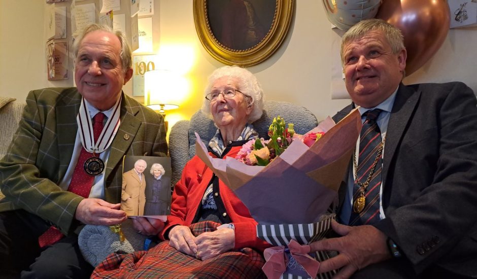 Jenny White seated in armchair flanked by Jimmy Denholm and Alan Watt with cards and flowers