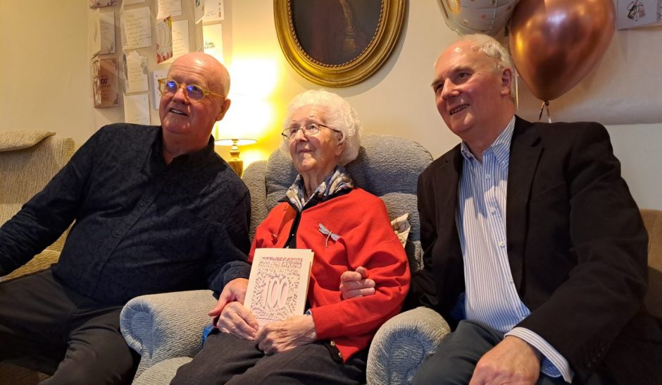 Jenny White seated in armchair flanked by her two sons
