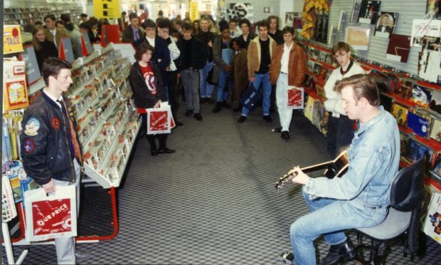 Shoppers look on as Edwyn Collins sits down with a guitar to perform at Our Price in Dundee in 1990.