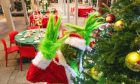 The Grinch posing in a mischievous way by the Christmas tree.