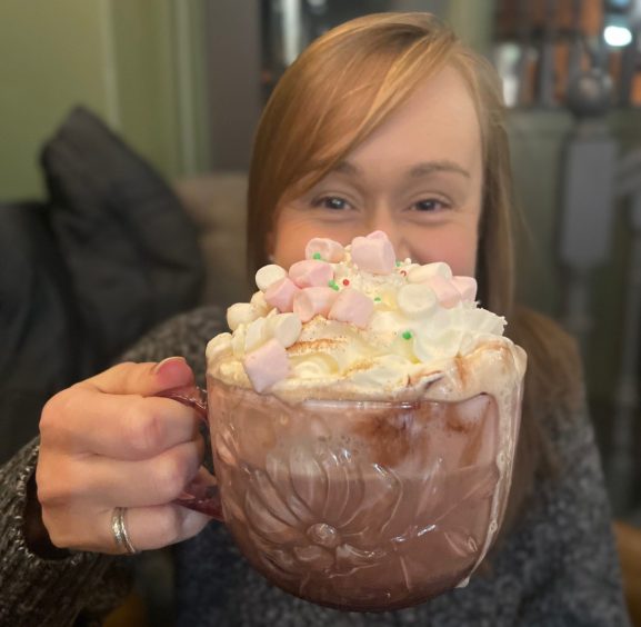 A woman holding up a huge mug of hot chocolate in front of her face.