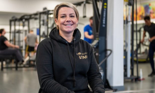 A smiling Fiona Oxley sitting on some equipment inside a gym