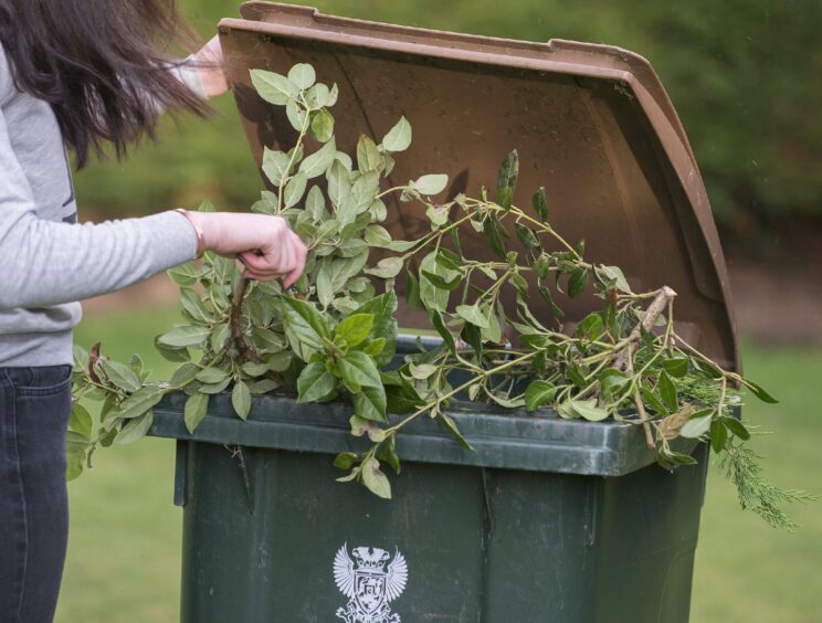 Woman putting garden waste into brown lidded bin with Perth and Kinross Council logo