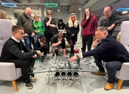 Group of people watching man and teenage boy play chess on set made from old Porsche parts at Y Centre in Perth