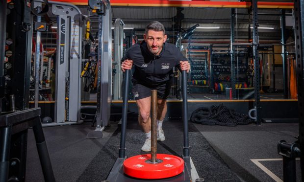 Club 300 gym owner and personal trainer Mike Lindsay poses for a picture using a piece of equipment