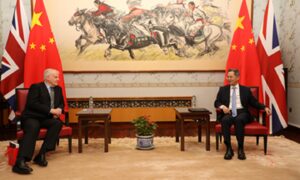 Alistair Michie sits in a grand room containing flags and a large painting as he receives the Chinese Government's friendship award from a Chinese official