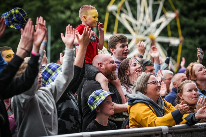 Crowd at front of stage at Heartland festival with small boy on father's shoulders and big wheel behind