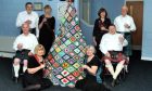 Group of people in kilts and formal dresses standing around crocheted Christmas tree