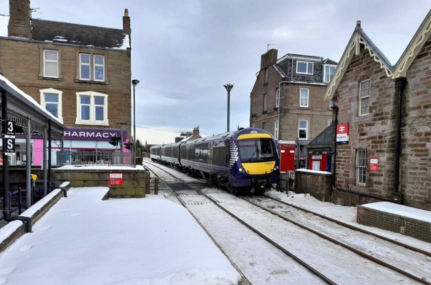 Class 170 unit 170414 arrives at Broughty Ferry level crossing in 2019, with shops and houses on either side.