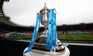 The Scottish Cup trophy on a platform with the inside of an empty Hampden Park in the background