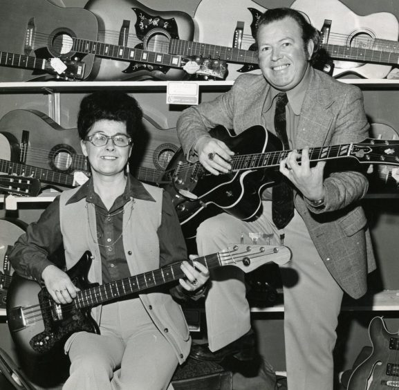 Smiling Vince and Eleanor Chalmers hold guitars