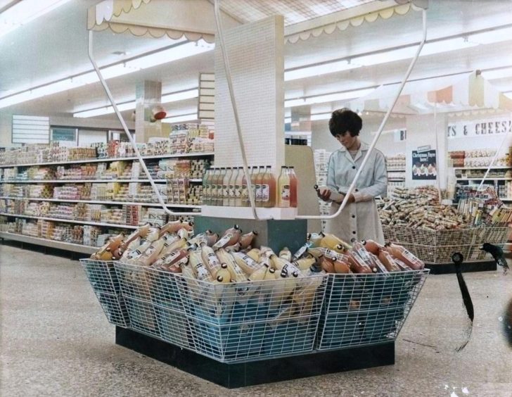 a woman looks at an item beside the display at the new supermarket in 1965. 