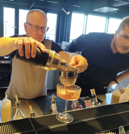 a staff member looks on as Brian has a go at making some cocktails.