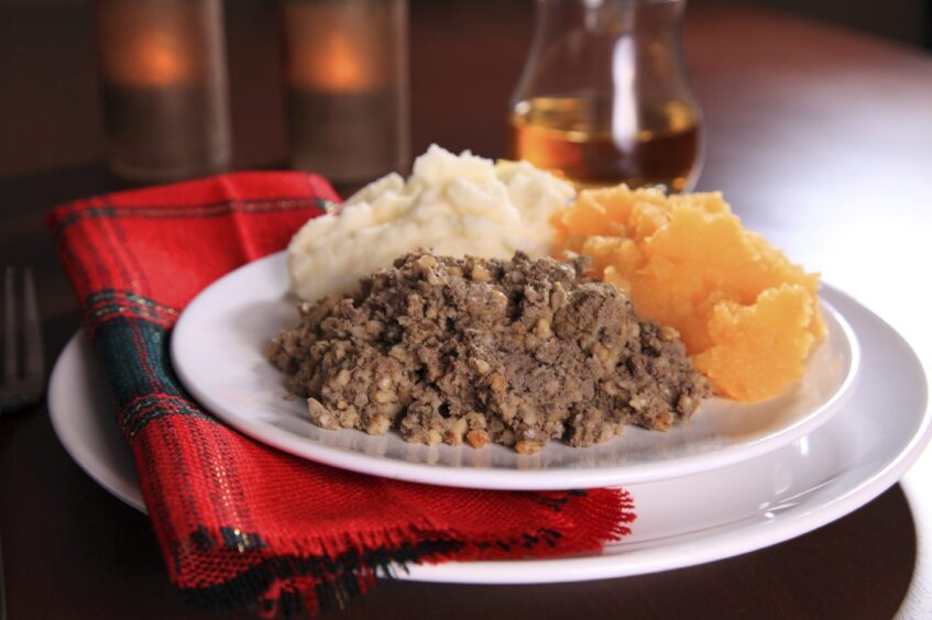 Plate of haggis, mashed potatoes and turnips on table with glass of whisky behind.