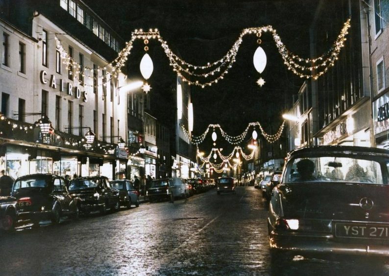 cars parked beneath a city street brightened by Christmas lights