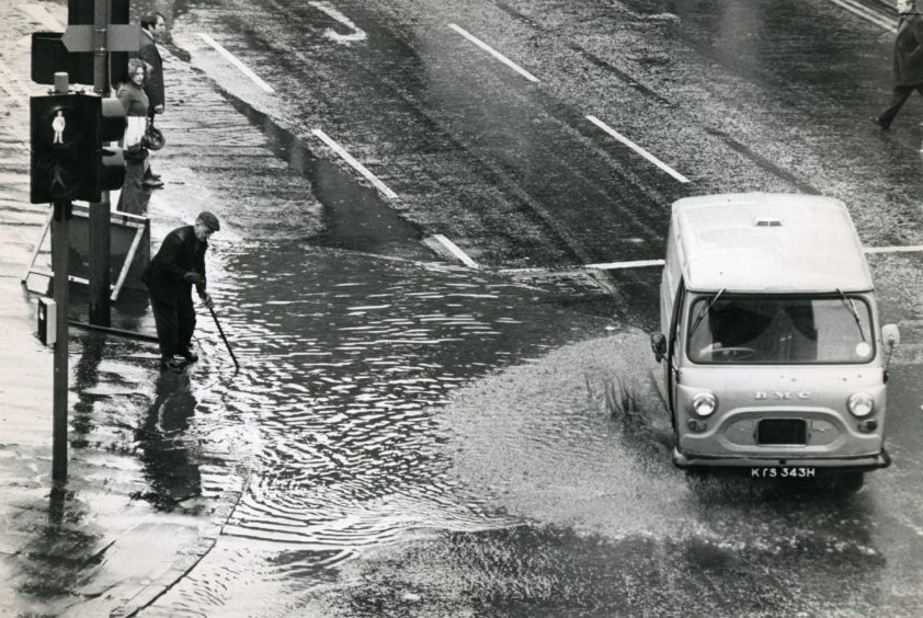 a van dries by as a man tries to clear a choked drain during the flooding in Dundee in 1975. 