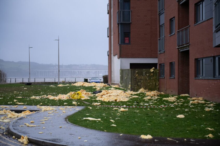 Insulation is scattered across the ground beside the building damaged by Storm Eowyn, with the River Tay in the background