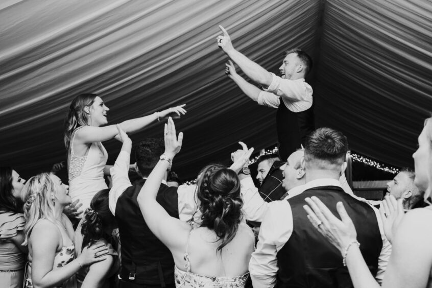 Black and white image of wedding couple being lifted on the dancefloor