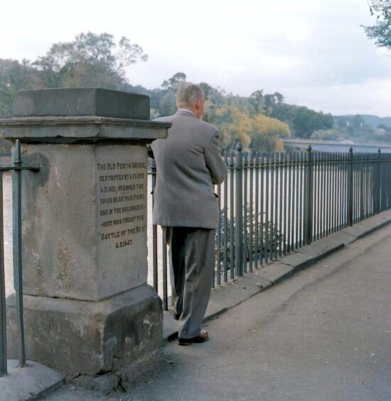 A man standing beside the old Perth Bridge marker. 