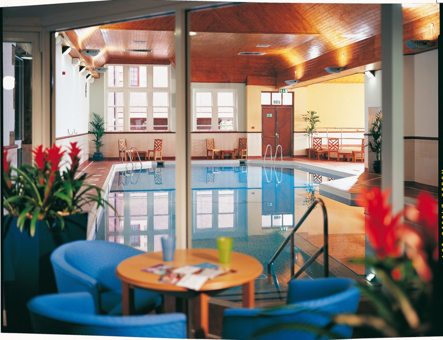 The swimming pool inside Stirling Highland Hotel, with a round table and three blue armchairs in the foreground