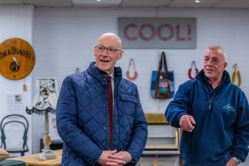 John Swinney and Alfie Ianetta inside Tayside Upcycling Craft Centre in front of a display of furniture, bags and a large sign which reads 'COOL!'