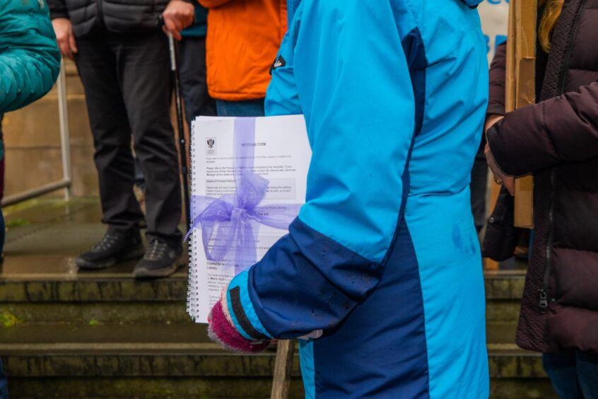 Libraries campaigner holding bundle of papers tied up with blue bow on steps of Perth and Kinross Council HQ.