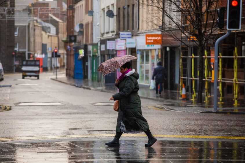 a woman with an umbrella walks along a quiet Perth street during the storm